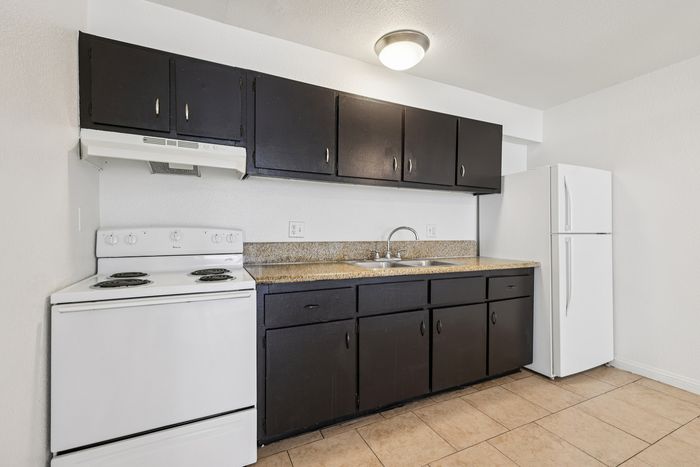 Modern kitchen with sleek dark cabinetry, spacious countertops, and a convenient white appliance set pairing perfectly with tile flooring.