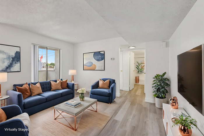 Modern living room with elegant decor, featuring blue seating, copper accents, and bright natural light.