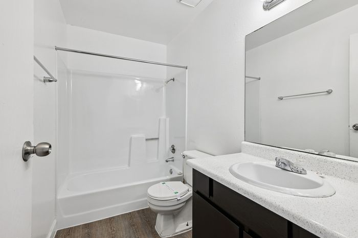 Modern bathroom with sleek white fixtures, a spacious bathtub, and elegant wood flooring, offering a serene retreat.