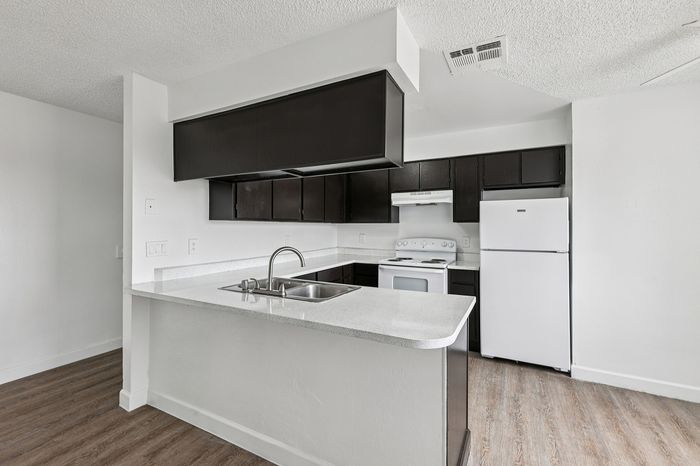 Modern kitchen with sleek dark cabinetry, white countertops, and stainless steel sink, offering a stylish and functional space for culinary creativity.
