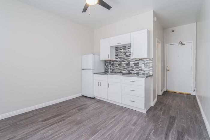 Modern apartment kitchen with sleek white cabinets, stylish backsplash, and dark wood laminate flooring.