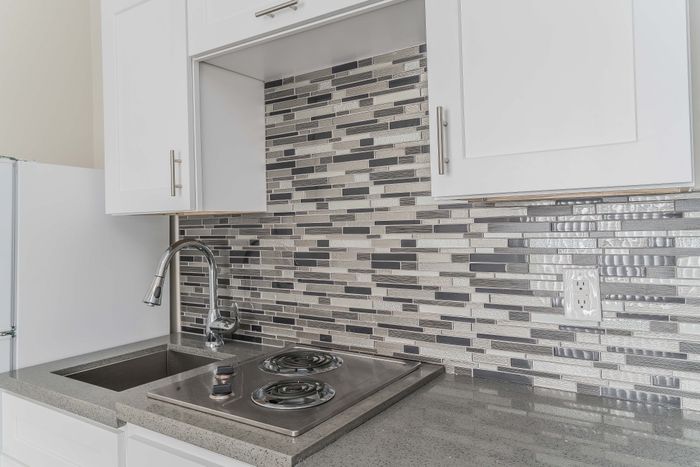 Modern kitchen design with sleek mosaic backsplash, elegant white cabinetry, and efficient cooktop.