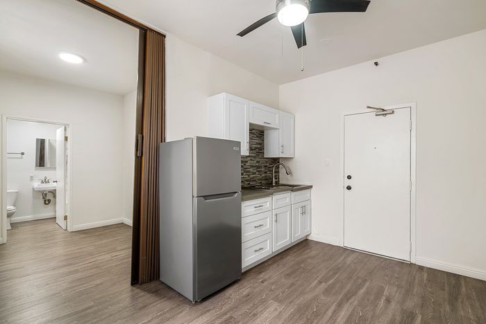 Modern apartment interior showcasing a sleek kitchenette with white cabinetry, stainless steel fridge, and stylish backsplash, adjacent to a bright bathroom entrance.