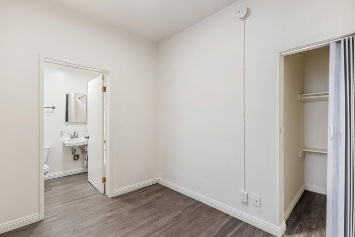 Bright and inviting bedroom with sleek hardwood flooring, featuring a compact, stylish bathroom and a spacious closet.