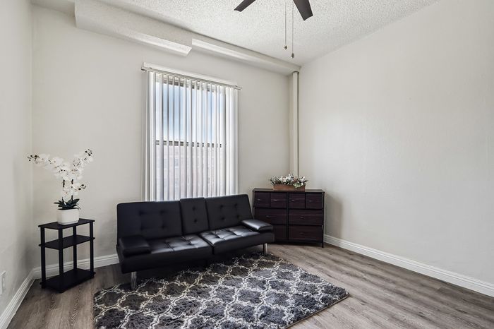 Bright and modern living room featuring a sleek black sofa, elegant rug, and large window with vertical blinds. Minimalistic decor enhances spacious feel.