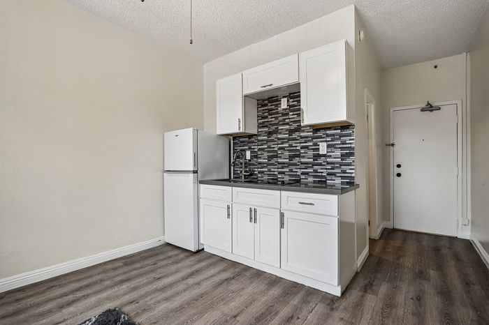 Modern kitchen with sleek white cabinetry, stylish backsplash, and elegant wood flooring in a bright apartment.