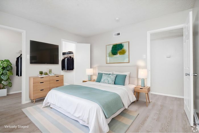 Bright and modern bedroom featuring elegant decor, a comfortable bed with teal accents, sleek furniture, and a flat-screen TV, offering a serene and stylish retreat.