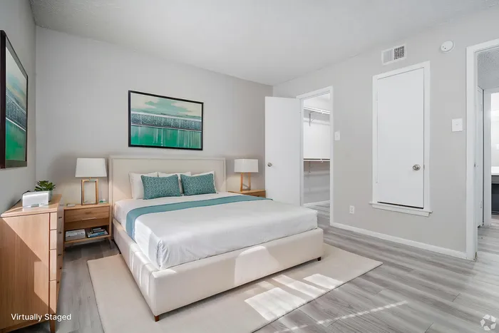 Virtually staged bedroom with modern decor, highlighting a comfortable bed, sleek nightstands, and vibrant artwork, offering a glimpse of a spacious walk-in closet.