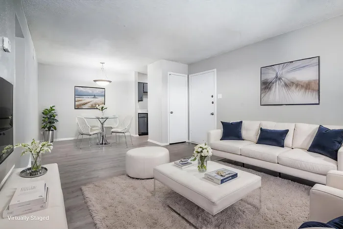 Chic and modern living room with plush white sofa, blue accent pillows, and elegant glass dining set in open-concept layout.