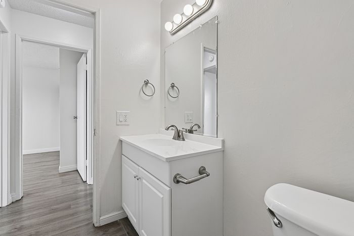 Modern bathroom with sleek white vanity, large mirror, and elegant lighting, featuring a stylish faucet and durable flooring.