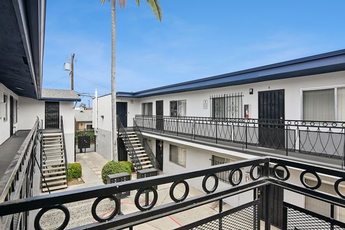 Modern apartment complex with stylish wrought iron railings, showcasing an open corridor and lush tropical touches under a clear blue sky.