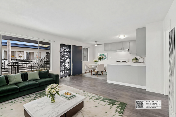 Chic open-concept living space with elegant green velvet couch, modern kitchen, and inviting dining area, enhanced by abundant natural light.