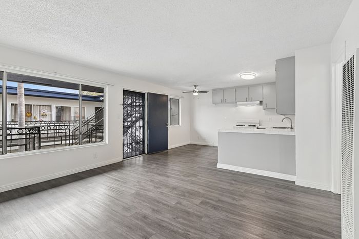 Bright and spacious living area with modern gray flooring and a sleek kitchen, featuring ample natural light from large windows.