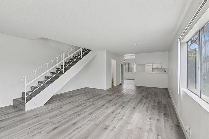 Bright, open floor plan apartment featuring elegant wood flooring, a modern staircase, and ample natural light from large windows.
