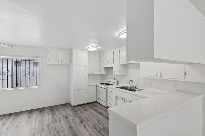 Bright and modern kitchen with white cabinetry, a double sink, and sleek built-in stove, set against elegant light wood flooring.