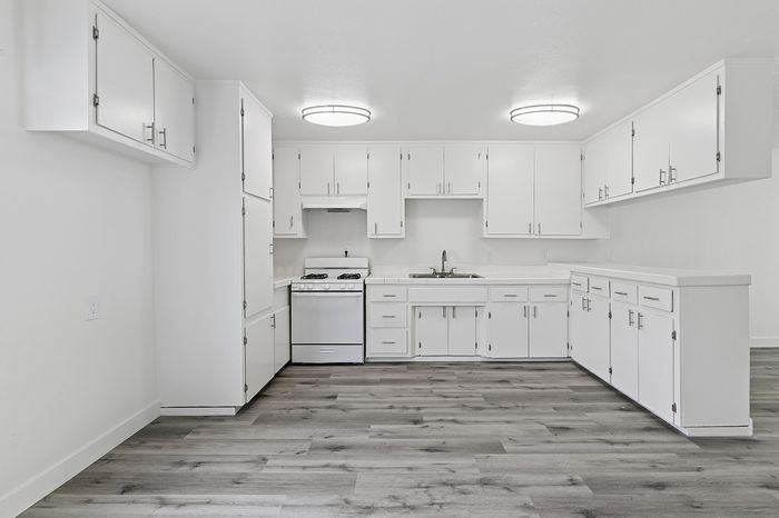 Bright modern kitchen with sleek white cabinetry and stainless steel stove, complemented by stylish wood flooring.