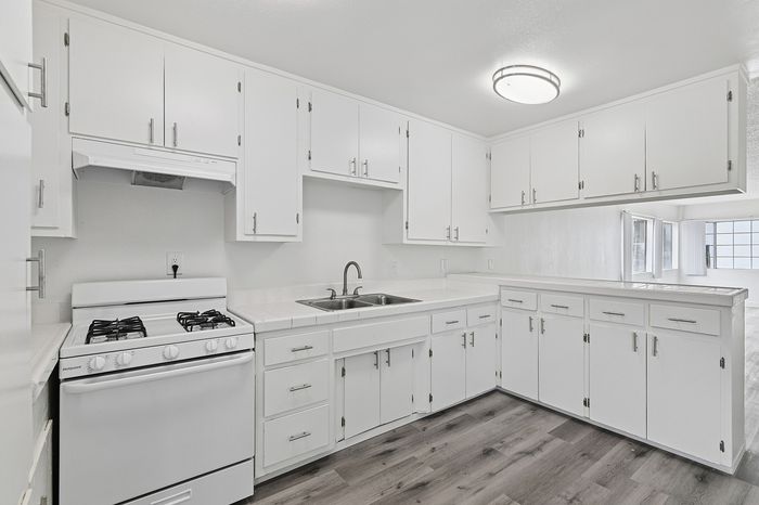 Bright and airy kitchen with sleek white cabinetry, modern gas stove, and elegant wood-style flooring, perfect for culinary enthusiasts.