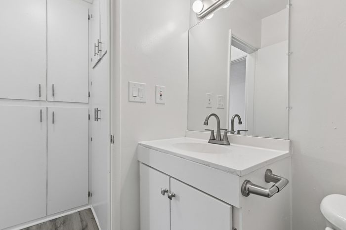 Modern bathroom with sleek white cabinetry, elegant faucet, and large mirror, reflecting contemporary design.