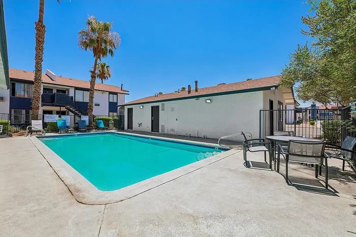 Inviting apartment complex pool area with lounge chairs, palm trees, and a clear blue sky.