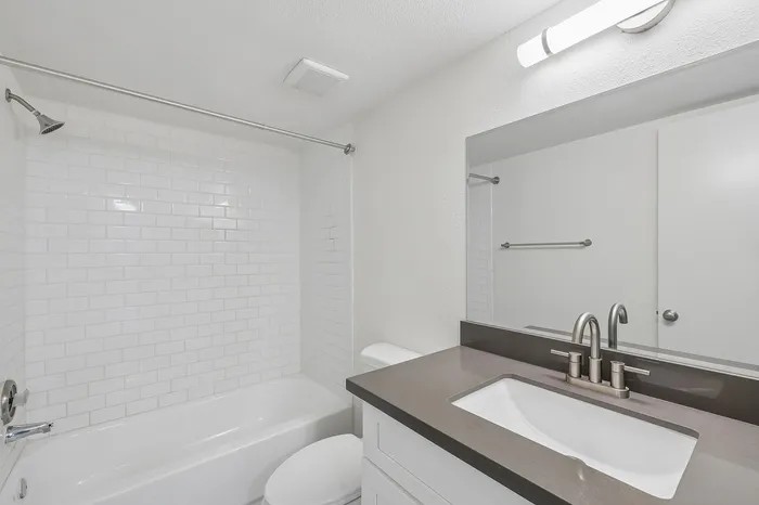 Modern bathroom featuring a sleek vanity with a stylish faucet, bright wall lighting, and a pristine white bathtub surrounded by subway tiles.