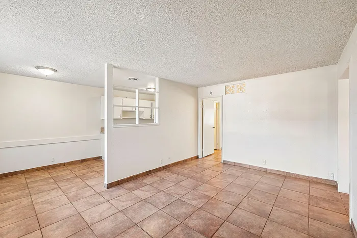 Inviting open-concept apartment with tile flooring, bright white walls, and glimpse of a modern kitchen.