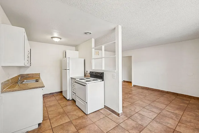 Bright, open-plan kitchen with elegant tiled flooring, modern appliances, and sleek countertops leading into a spacious living area.