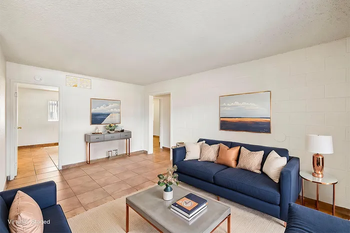 Bright and inviting living room with modern blue sofas, elegant decor, and natural light streaming in, creating a cozy ambiance. Virtually staged for inspiration.