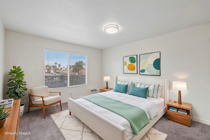 Chic bedroom with modern decor, large window view, and vibrant artwork in a virtually staged setting.