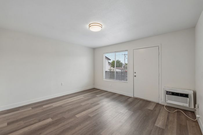 Bright and modern living area with elegant hardwood flooring, large window, and stylish ceiling light, perfect for cozy relaxation.