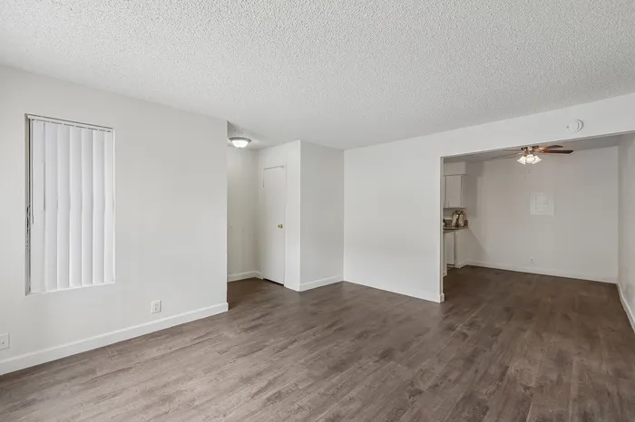 Inviting living space with elegant wood flooring and ample natural light, opening into a cozy kitchen area. Ideal for modern living.