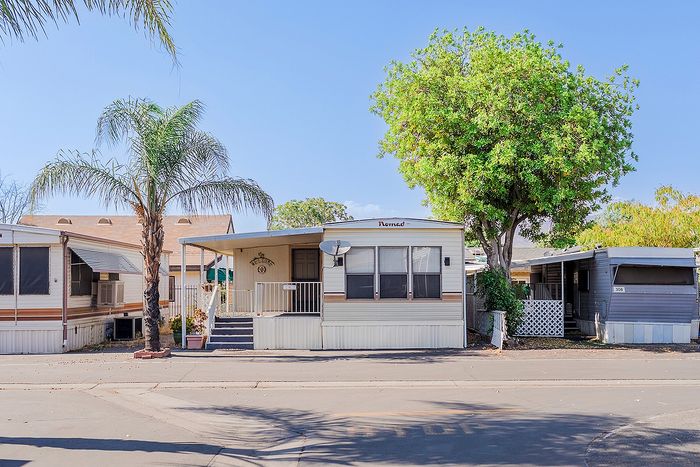Charming mobile home nestled in a serene neighborhood with lush palm trees, offering a cozy and inviting outdoor space.