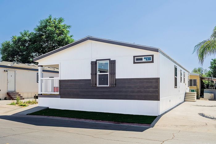 Modern mobile home with sleek wood accents and a welcoming front porch, nestled in a sunny, serene neighborhood.