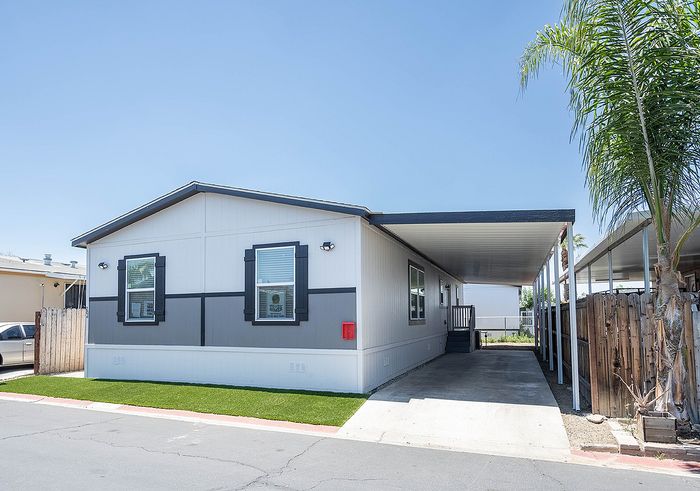 Modern manufactured home with sleek exterior design, covered driveway, and manicured front lawn, offering spacious outdoor living.