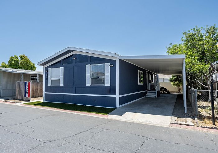 Charming mobile home with modern exterior, featuring a sleek blue facade, white trim, and a spacious covered carport, ideal for comfortable residential living.