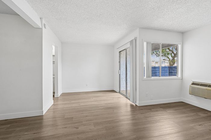 Bright and open living space with modern wood flooring, large windows, and a sliding glass door leading to a private patio.