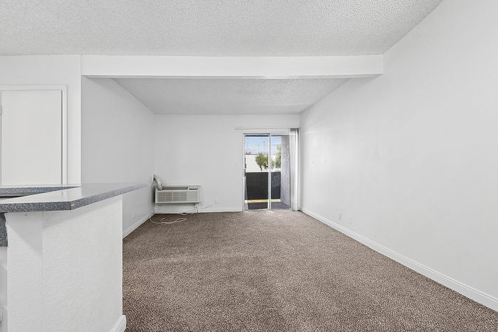 Bright and inviting living area with plush carpeting, sliding glass door leading to a balcony, and a cozy atmosphere perfect for relaxation.