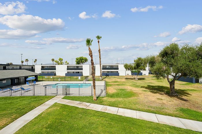 Beautiful apartment complex with a refreshing swimming pool, manicured lawns, and bright blue skies, offering a perfect blend of relaxation and modern living.
