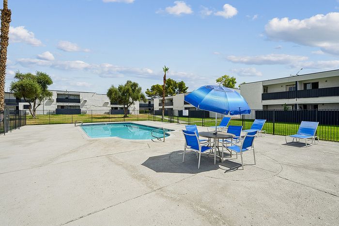 Inviting outdoor leisure area with a sparkling pool, blue sun umbrellas, and comfortable loungers, perfect for a relaxing day under the sun.