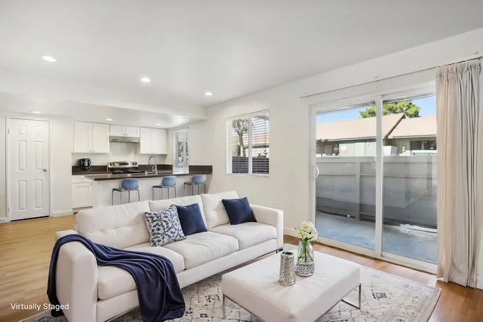 Bright open-concept living area with a sleek modern kitchen, cozy white sofa, and large sliding glass doors leading to a private balcony, creating a warm and inviting atmosphere.