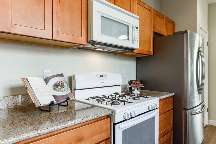 Kitchen featuring white microwave installed over white gas range and stainless steel regrigerator.