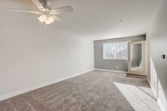 Large open room with plush carpeting and a ceiling fan with a door leading out to the patio