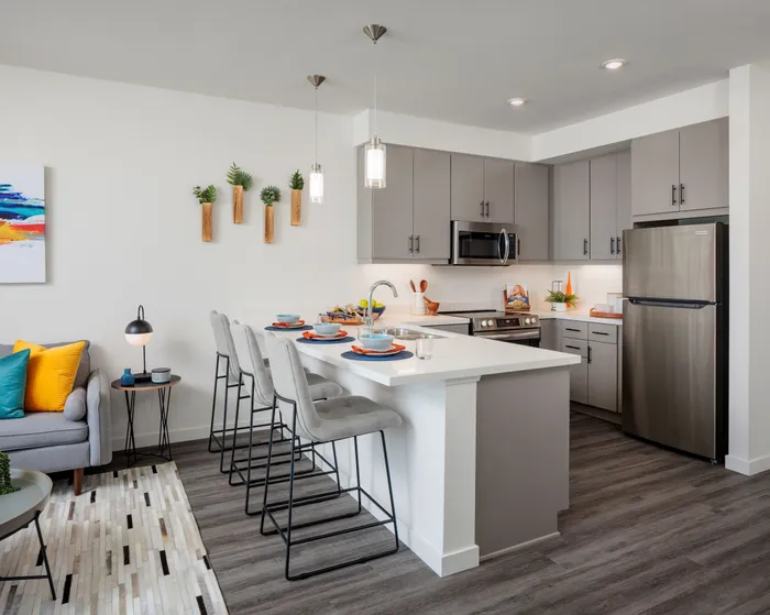 Apartments for Rent in La Mesa, CA - Kelvin - Kitchen with Luxury Wood-Style Flooring, Breakfast Bar, Bar-Style Chairs, Pendant Lights, Stainless Steel Appliances, Grey Flat-Panel Cabinetry, and White Quartz Countertops.