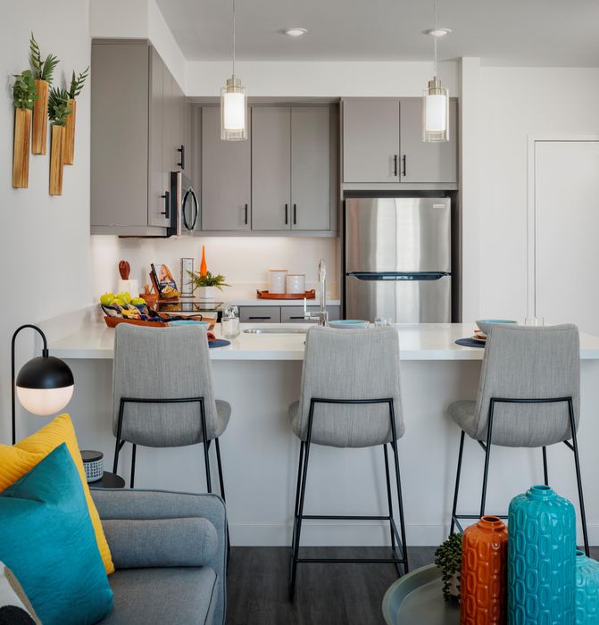 Staged l-shaped kitchen with peninsula featuring lvp flooring, brand new stainless steel appliances, and quartz countertops with 3 breakfast bar seats