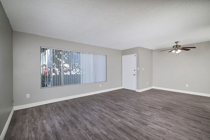 Living room with large window with window coverings, ceiling fan, and vinyl flooring