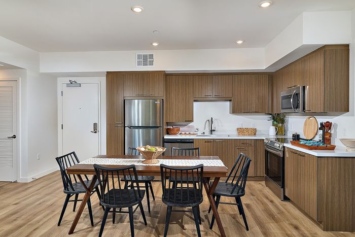 Serra Mesa, San Diego, CA, Apartments With In-Unit Washer and Dryer - DEZI - Kitchen With Wood Cabinets, Quartz Countertops, Stainless Steel Appliances, and Dining Table Under Recessed Lights.