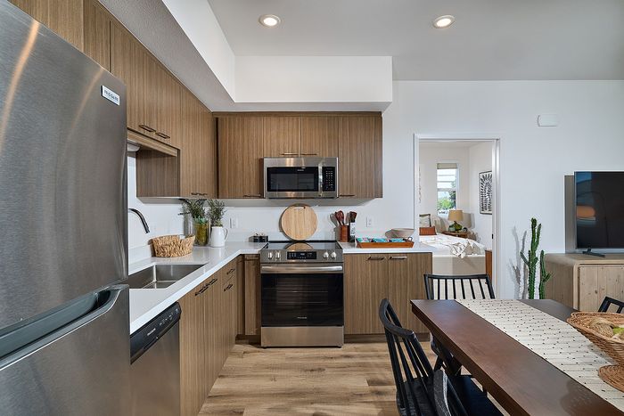 Serra Mesa, San Diego, CA Pet-Friendly Apartments - DEZI - Kitchen with Tall Ceilings, Durable Vinyl Plank Flooring, Quartz Countertops, Stainless Steel Appliances Including Hood-Mounted Microwave and Dishwasher, Flat-Panel Kitchen Cabinets, and 6-Seater Dining Table.