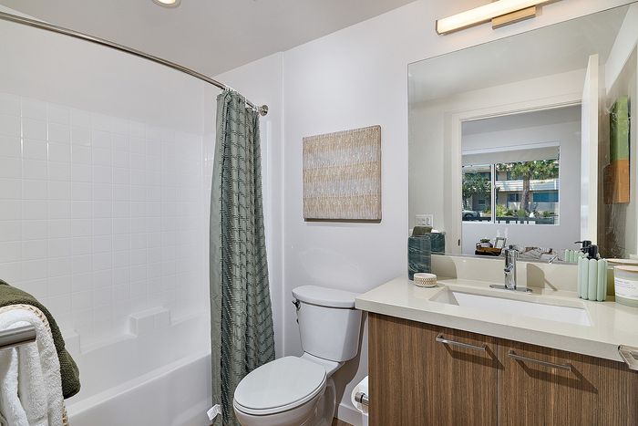 Pet-Friendly Apartments in Serra Mesa, San Diego, CA - DEZI - Bathroom with Bathtub, Shower Curtain, Towel Bar, Wooden Sink Cabinet, Light Fixture, Mirror, Sink, and Wall Art