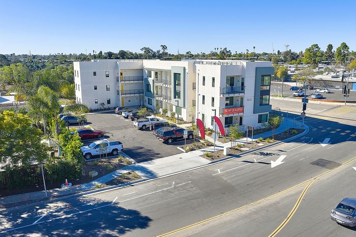 2-Bedroom Apartments in Serra Mesa, San Diego, CA - DEZI - Aerial View of Apartment Community With Parking Lot, Multi-Story Buildings, and Street Corner Entrance.