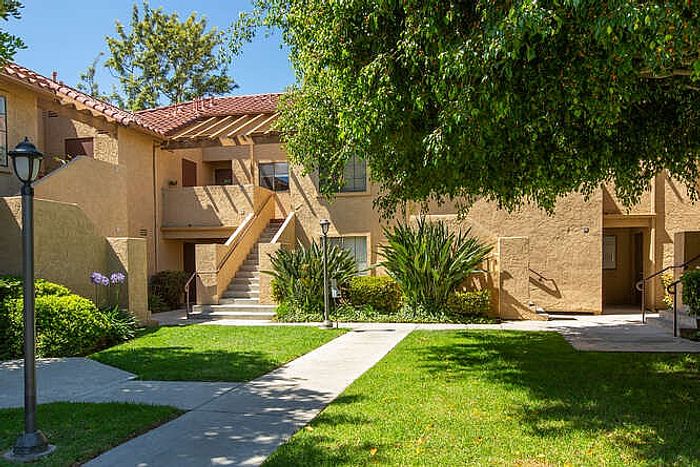 A wide concrete walkway leading through a manicured green lawn and professional landscaping toward the apartment entrances.