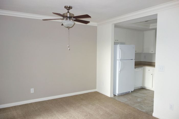 A functional dining or living space with neutral carpet, a ceiling fan, and a view into the kitchen area.
